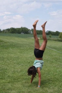 A girl doing a handstand on green grass.