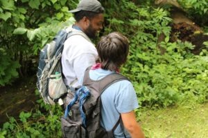 Two individuals wearing backpacks in the woods.