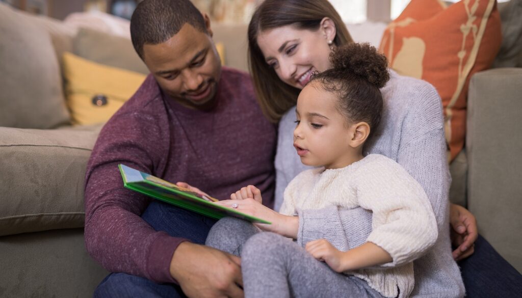 Padre afroamericano, madre caucásica y niño mixto leyendo un libro juntos.