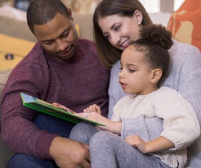 African American Father, Caucasian Mother, and mixed child reading a book together.