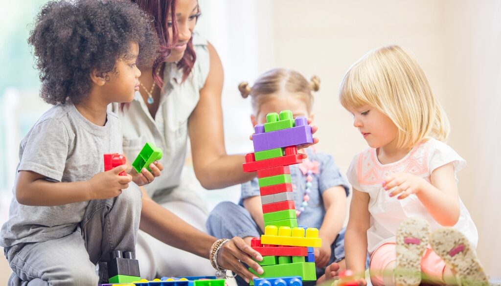Niños pequeños en blanco y negro construyendo torres con bloques con un adulto.