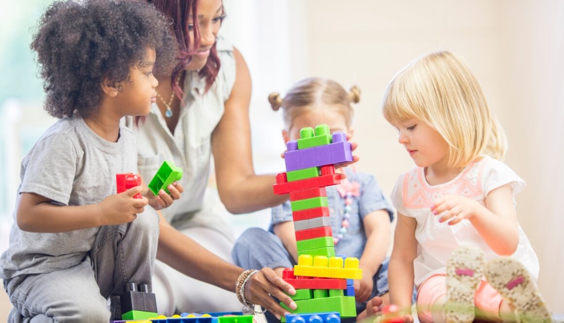 Young black and white children building towers with blocks with an adult.