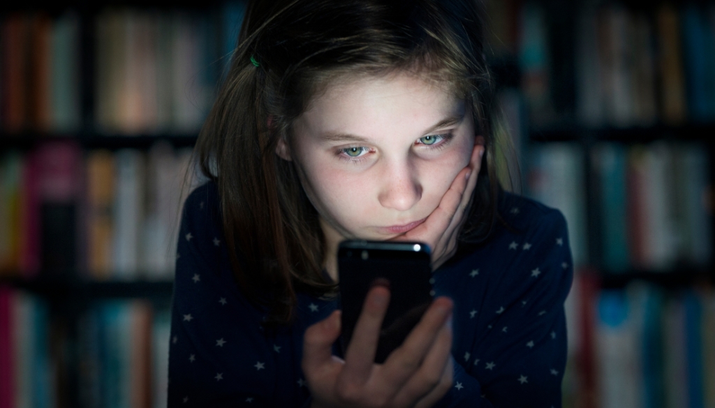 Una niña blanca leyendo comentarios de intimidación en línea en un teléfono.