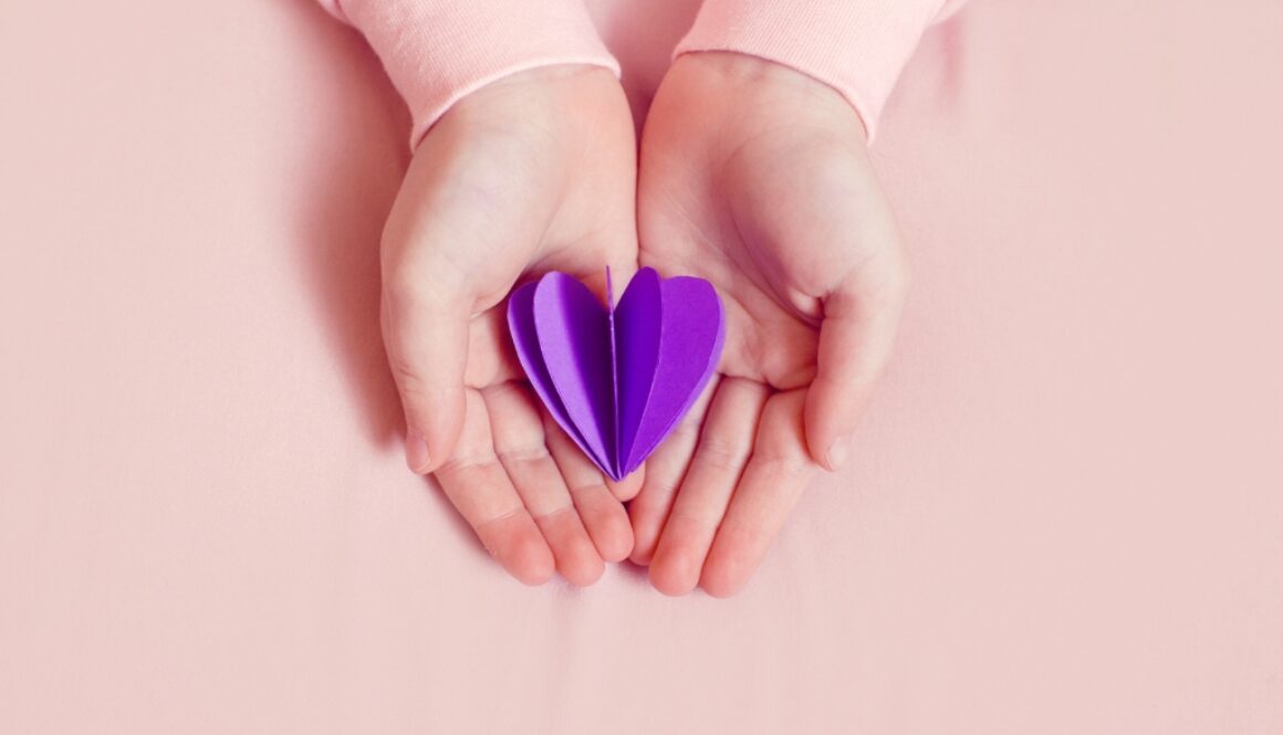 A white girls hands holding a paper purple heart shape.