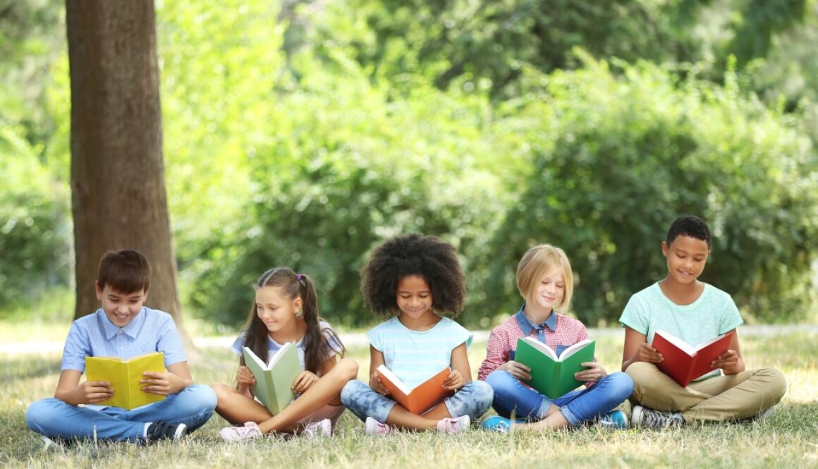A small group diverse children reading books outside to improve habits.