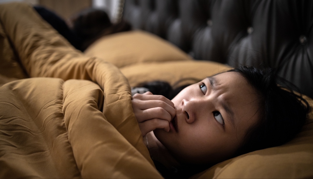 A teenage Asian girl laying in bed trying to manage childhood anxiety.