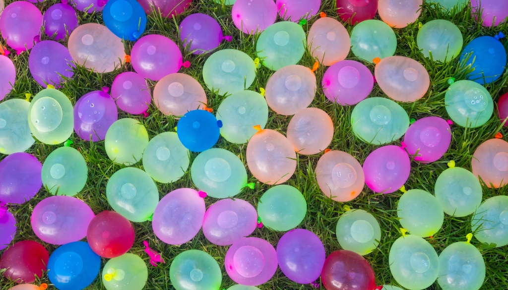 Colorful water filled balloons laying in grass.