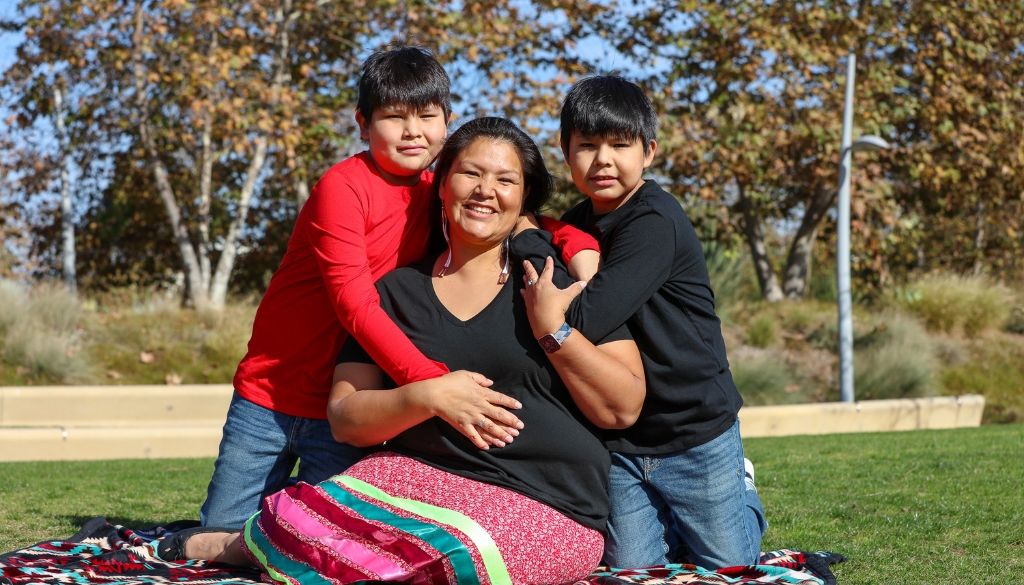 Native American Mother smiles on a blanket with her two children.